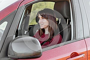 Pretty youDark-haired smiling girl in a burgundy sweatshirt driving a teracotta car