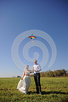 Pretty young adult wedding couple walking on field with kite