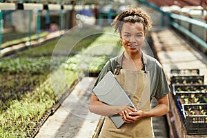 Pretty young African American female with laptop standing in greenhouse photo