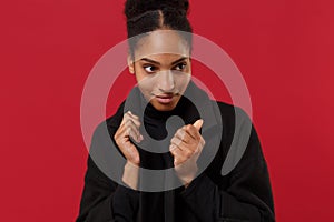 Pretty young african american woman girl in black coat posing isolated on bright red wall background studio portrait