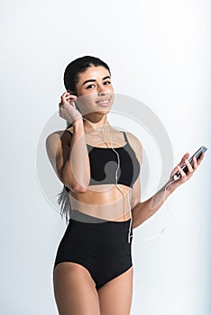 Young african american woman listening music in earphones, smiling and looking at camera on white