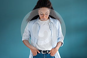 Pretty young african american woman looking down with serious expression while posing over blue background