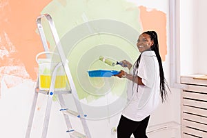 Pretty young african american woman with painting roller indoors. Redecoration, renovation, apartment repair and