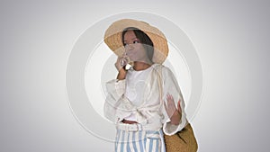 Pretty young african american woman in a straw hat talking on her phone on gradient background.