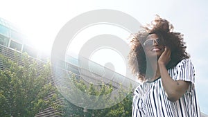 Pretty young african american woman in sunglasses talking on the phone. Sky background