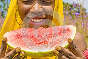 pretty young african lady enjoying a delicious slice of watermelon fruit outside