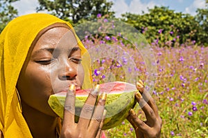 pretty young african woman eating watermelon outside