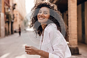 Pretty young african woman looking at distance with wide smile spends time outdoor in spring day.