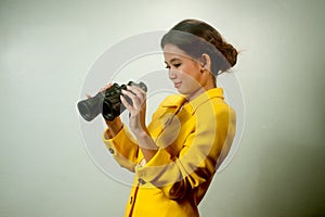 Pretty young Asian businesswoman in yellow suit holding a binoculars.