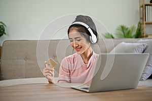 Pretty young Asian female wearing headphones, holding a credit card. Online shopping concept