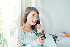 Pretty young asian woman drinking green fresh vegetable juice or