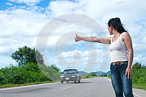 Pretty young Asian woman with hand up calling passing car.