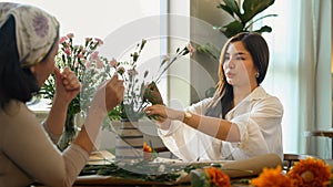 Pretty young asian woman and her senior mother making a bouquet with fresh flowers at floral shop. Small business