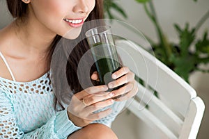 Pretty young asian woman holding green fresh vegetable juice or