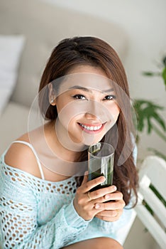 Pretty young asian woman holding green fresh vegetable juice or