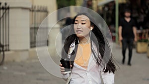 Pretty young asian woman listening to music with headphones on her smartphone while walking down the street. Leisure