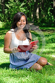 Pretty young Asian woman reading in park