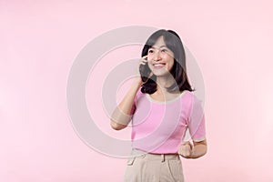 Pretty young asian woman showing success, victory hand gesture while receiving great news from smartphone on pink background.