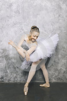 Pretty young ballerina dancer dancing classical ballet against rustic wall