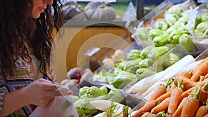 Pretty young beautiful girl or woman buys food, picks carrots, cabbage, lettuce, cauliflower in the market, in the