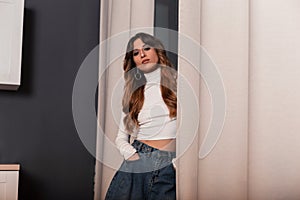 Pretty young beautiful woman with long red hair in a stylish T-shirt in fashionable blue jeans posing near vintage curtains