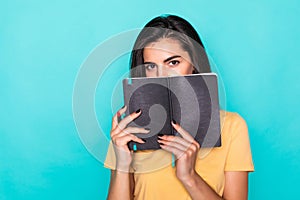 Pretty young beautiful woman standing, writing, take notes, holding textbook notebook organizer in hand and pen on turquoise