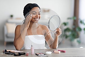 Pretty young black woman applying make up and smiling