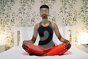 pretty young black woman doing meditation exercises on her bed at home