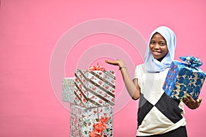 pretty young black woman holding a gift box and pointing to more gift boxes