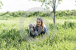 Pretty young blond woman resting with fluffy gray dog on green lawn in summer
