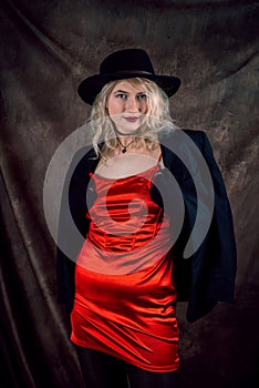 pretty young blond woman wear red evening dress and black hat isolated on dark background