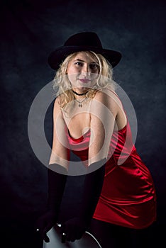 pretty young blond woman wear red evening dress and black hat isolated on dark background
