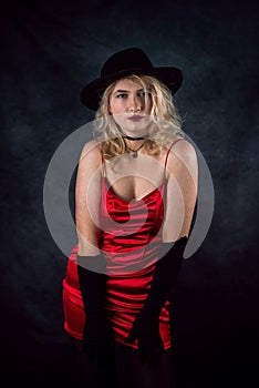 pretty young blond woman wear red evening dress and black hat isolated on dark background