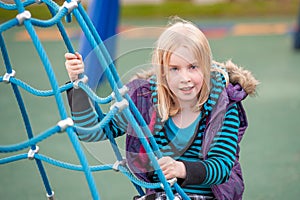 Pretty young blonde girl climbing on a rope ladder in a playground