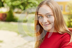 Pretty young blonde girl with green eyes, thin lips, dimples on cheeks and freckles on face wearing red clothes looking happily in