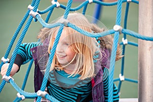 Pretty young blonde girl playing on a rope climbing frame