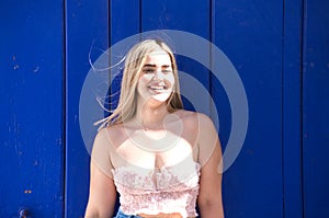 Pretty young blonde woman with a blue door in the background makes different expressions and has fun smiling. Conceptual happiness