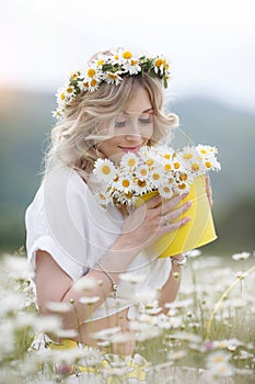 Pretty young blonde woman with camomiles in white blooming field. girl in camomile wreath