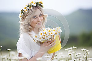 Pretty young blonde woman with camomiles in white blooming field. girl in camomile wreath