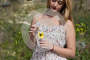 Pretty young blonde woman defoliate a yellow daisy. The woman is playing he loves m