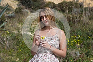 Pretty young blonde woman defoliate a yellow daisy. The woman is playing he loves m