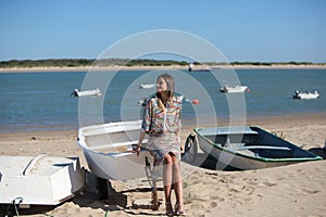 Pretty young blonde woman sitting in the fishermen's boats on the seashore. In the background on the horizon the blue sea