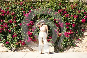 Pretty young blonde woman wearing sunglasses and dressed in embroidered trousers and crocheted top, enjoys sunny day. In the