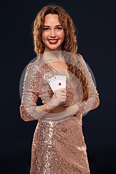 Pretty young brown-haired woman in golden cocktail dress holding pair of aces and smiling