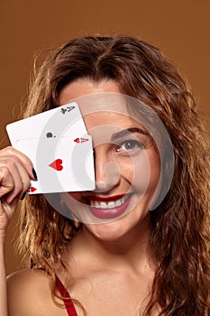 Pretty young brown-haired woman in red cocktail dress holding pair of aces and smiling