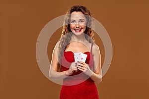 Pretty young brown-haired woman in red cocktail dress holding pair of aces and smiling