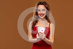 Pretty young brown-haired woman in red cocktail dress holding pair of aces and smiling