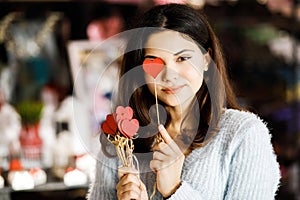 Pretty young brunette girl chooses decor for Valentine`s Day. Girl holding red hearts on a stick, festive decor