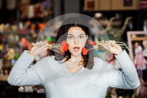 Pretty young brunette girl chooses decor for Valentine`s Day. Girl holding red hearts on a stick, festive decor