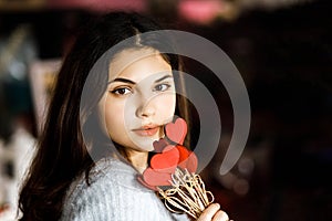 Pretty young brunette girl chooses decor for Valentine`s Day. Girl holding red hearts on a stick, festive decor